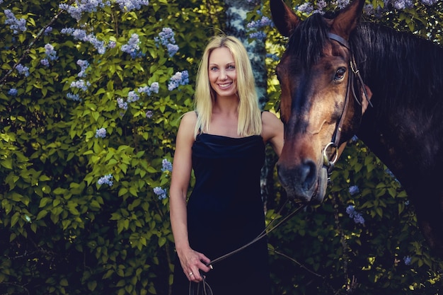 Smiling blond female in black dress and her brown horse.