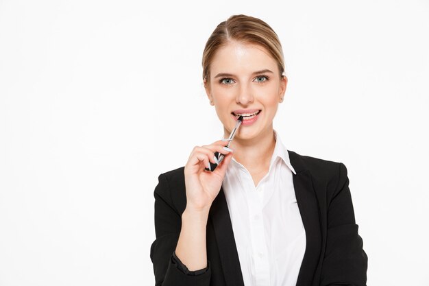 Smiling blonde business woman bites pen and  over white wall