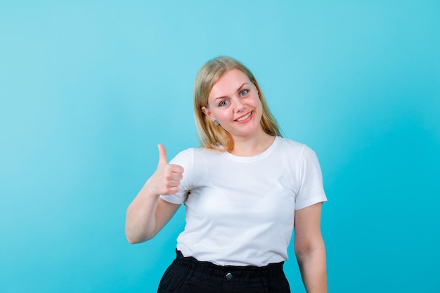 Smiling blonde girl is showing perfect gesture on blue background