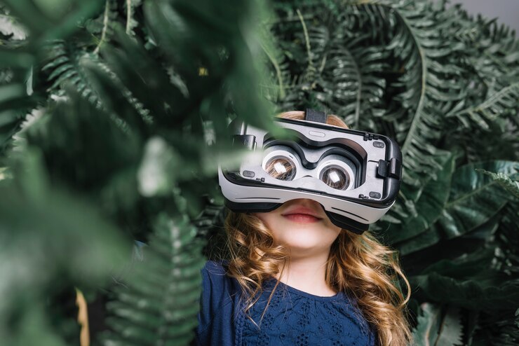 Free Photo smiling blonde little girl using virtual headset standing among the green plant