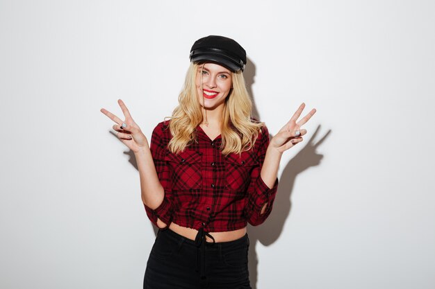 Smiling blonde woman in checkered shirt and cap showing peace