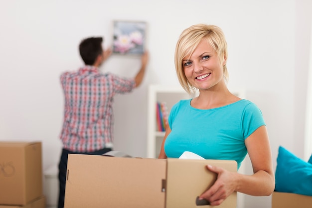Улыбающаяся блондинка женщина, держащая картонную коробку во время переезда домой