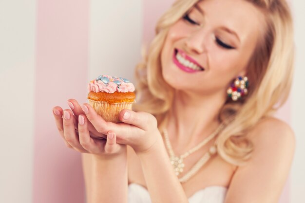 Улыбающаяся блондинка женщина, держащая небольшой кекс