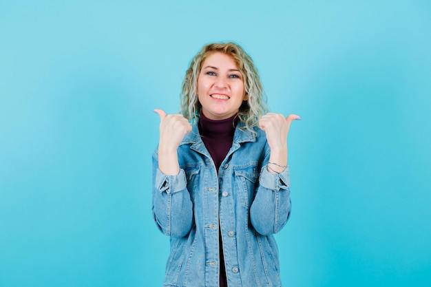 Smiling blonde woman is showing right and left with thumbs on blue background