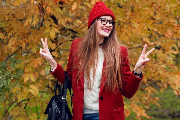 Smiling blonde woman with long hairs walking in sunny autumn park in trendy casual outfit.