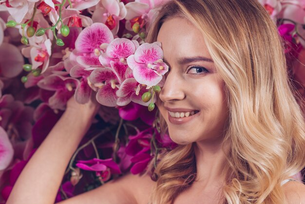 ピンクの蘭の枝と彼女の片目を覆っている笑顔金髪の若い女性