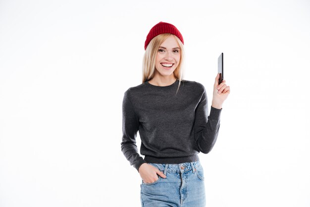 Smiling blonde young woman in hat standig and holding blank mobile phone