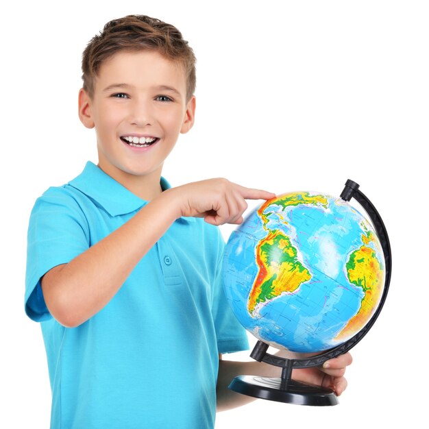 Улыбающийся мальчик в повседневной одежде держит глобус в руках и указывает на него на белом