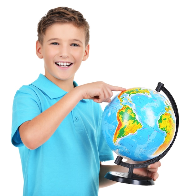 Smiling boy in casual holding globe with in hands and points on it isolated on white