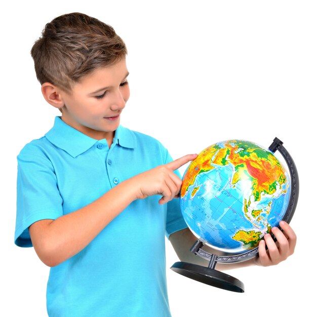 Smiling boy in casual holding globe with in hands and points on it isolated on white