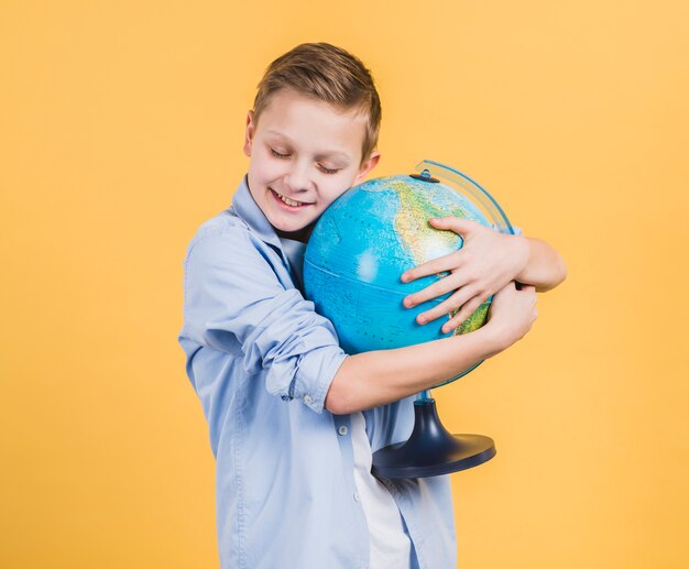 Smiling boy embracing globe hand against yellow backdrop