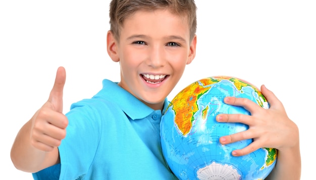 Бесплатное фото Улыбающийся мальчик в случайном холдинге земной шар с большими пальцами руки вверх знак - изолированные на белом