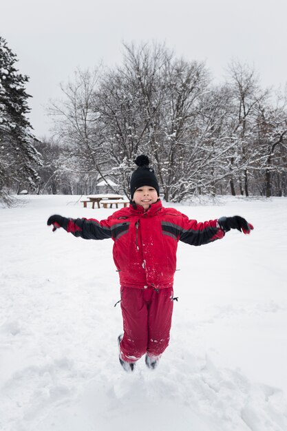 Il ragazzo sorridente che salta sulla terra nevosa nella stagione invernale