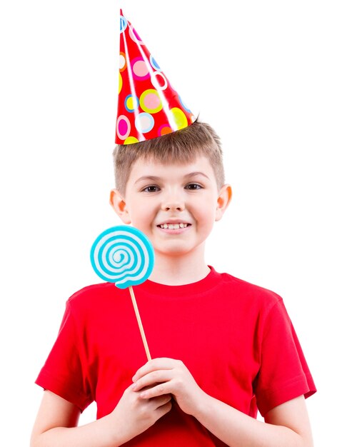 Smiling boy in red t-shirt and party hat holding colored candy - isolated on white