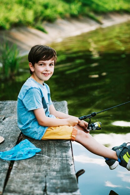 Улыбающийся мальчик, сидящий на пирсе, рыбалка над озером