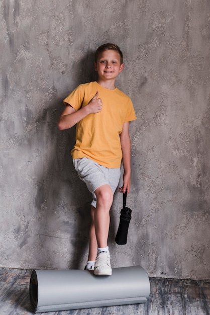 Foto gratuita ragazzo sorridente che sta davanti al muro di cemento che mostra i pollici su