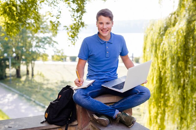 Улыбаясь мальчик, учиться с ноутбуком в парке
