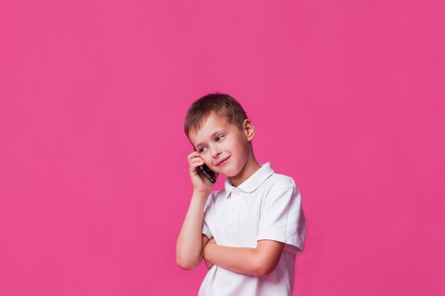 분홍색 벽 배경 위에 핸드폰에 웃는 소년