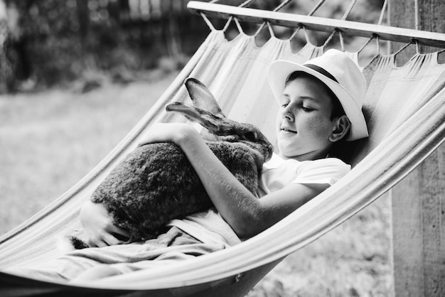Smiling boy wearing hat lying on hammock with rabbit