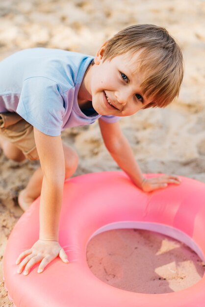Улыбающийся мальчик с плавательным кольцом на песке