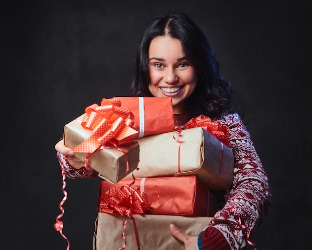 眼鏡と暖かいセーターで笑顔のブルネットの女性は、画像に明るい色の効果を持つクリスマスプレゼントを保持します。