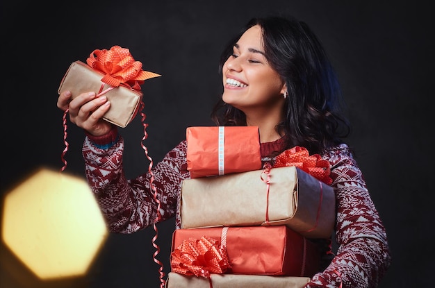 Foto gratuita una donna bruna sorridente con gli occhiali e un maglione caldo tiene i regali di natale con un effetto di colore brillante sull'immagine.