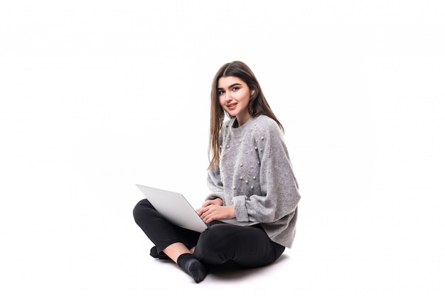 Smiling Brunette girl model in grey sweater sit on the floor and work studie on her laptop