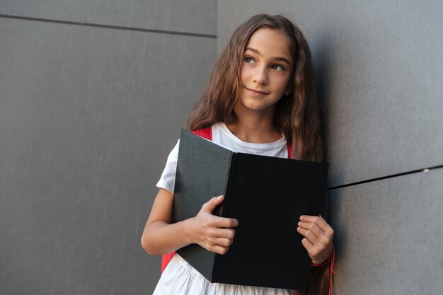 Smiling brunette schoolgirl with long hair holding book