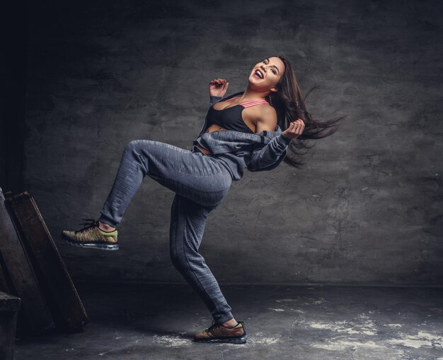 Smiling brunette woman in grey sportswear dancing on a grey background.