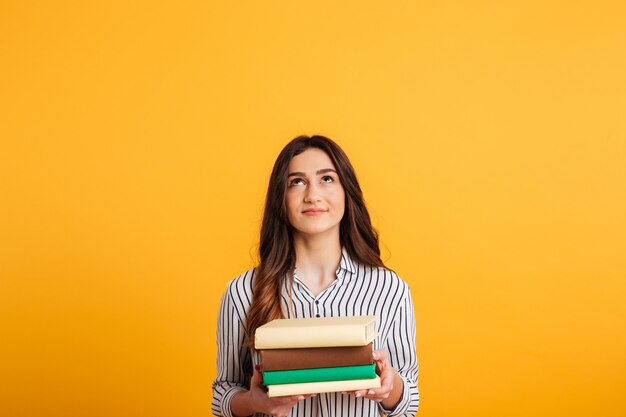 Smiling brunette woman in shirt holding books and looking up