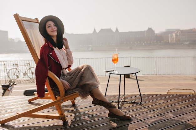 Улыбающаяся брюнетка женщина, сидящая на кресле, наслаждаясь отпуском в Европе
