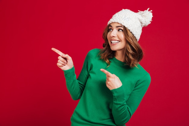 Foto gratuita donna sorridente del brunette in maglione e cappello divertente che indica via