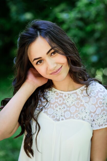 Smiling brunette woman in white dress poses in the garden