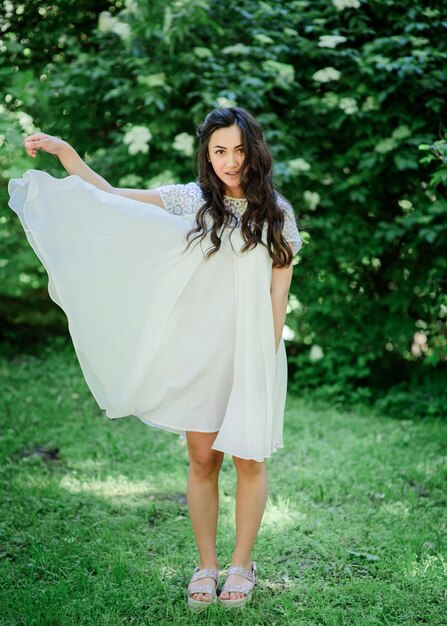 Free photo smiling brunette woman in white dress poses in the garden