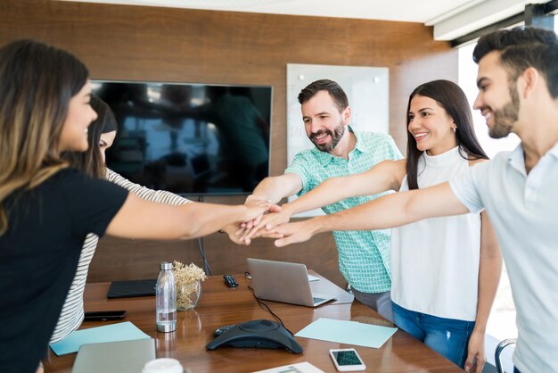 Smiling business colleagues with their hands stacked over table in meeting at office