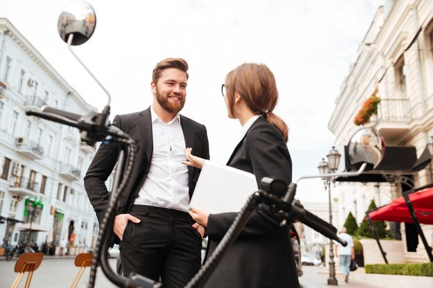 Smiling business couple posing near the modern motorbike outdoors