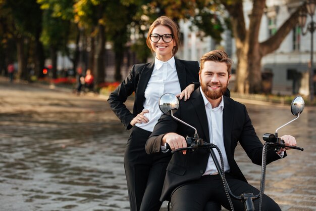 Smiling business couple posing with modern motorbike outdoors