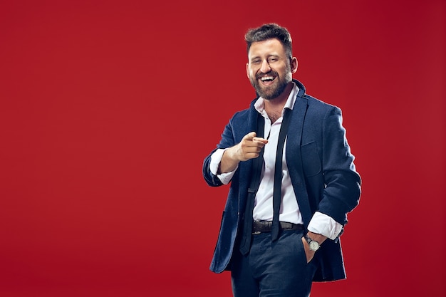 smiling business man point you, want you, half length closeup portrait on red studio background.