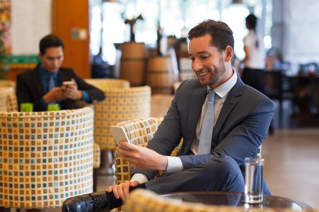 Smiling Business Man Texting on Smartphone in Cafe