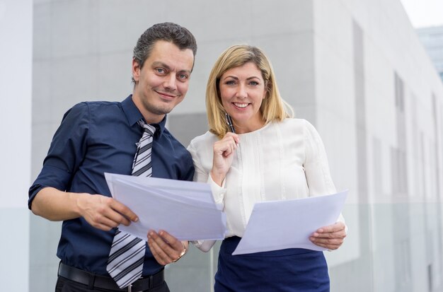 Smiling business man and woman discussing documents outdoors. 