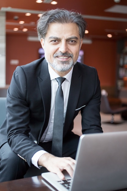 Free photo smiling business man working on laptop in lobby