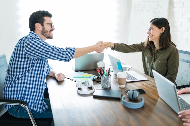 Smiling business partners shaking hands after successful deal at conference table in office