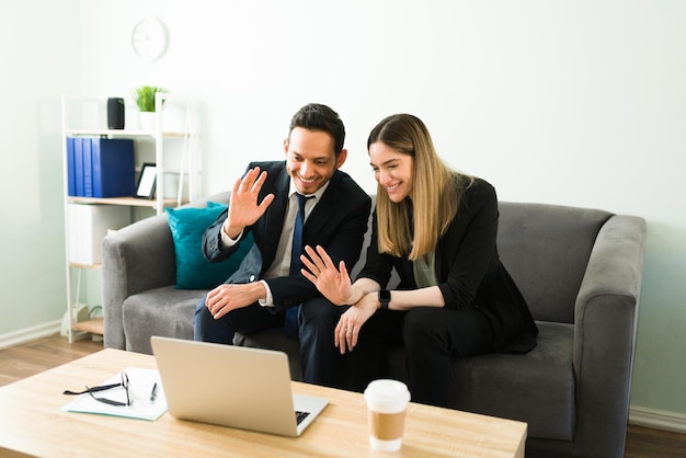 ノートパソコンでのビデオ通話中に、笑顔のビジネスパートナーが手を振って同僚や同僚に挨拶します。オフィスでのオンライン会議中のビジネスの女性と男性