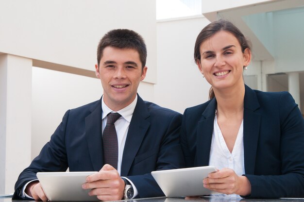 Smiling business people looking at camera and holding tablets