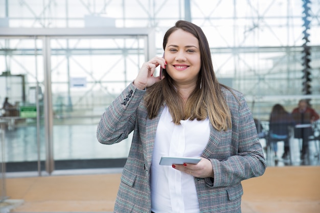 スマートフォンを屋外で呼び出すビジネス女性の笑みを浮かべてください。