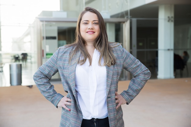 Free photo smiling business woman keeping hands on hips outdoors