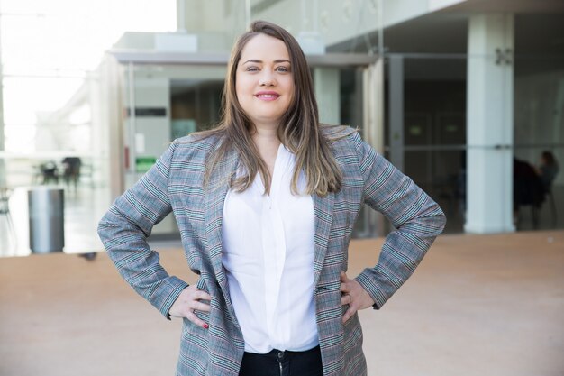 Smiling business woman keeping hands on hips outdoors