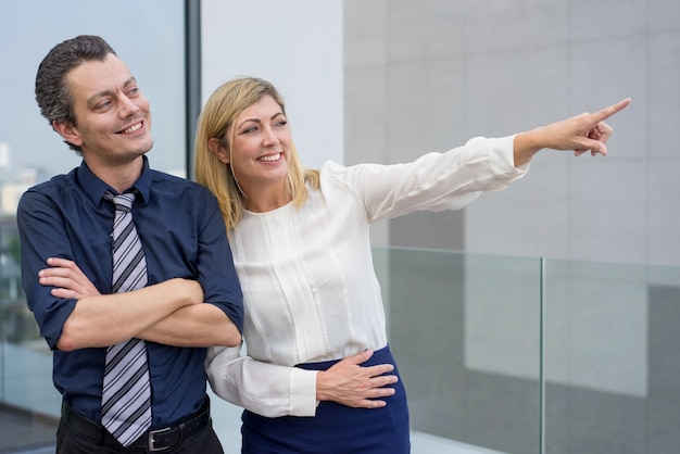 Smiling business woman showing male colleague something outdoors.