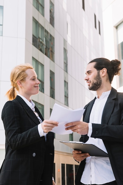 Smiling businessman and businesswoman holding paperwork in hands at outdoors