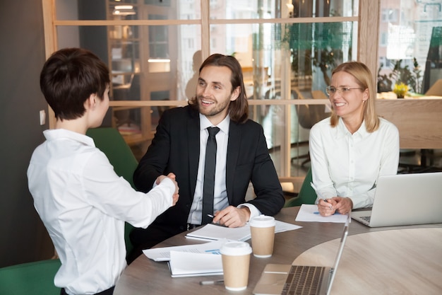 Smiling businessman and businesswoman shaking hands at group meeting negotiations